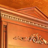 A custom solid cherry pediment sits atop the integrated refrigerator enclosure, and a heavy crown molding with egg & dart moldings below, along with carvings and split posts, all by Wood-Mode.