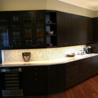 Doors with glass inserts display their extensive wine glass collection, while the under-cabinet wine chiller is conveniently located below. A stack of drawers holds all the bar supplies (the extra-deep bottom drawer holds liquor bottles upright and easy to get to). Under-cabinet and indirect lighting illuminate the space beautifully, while electrical outlets are neatly concealed below the upper cabinets. Kitchen Remodeling Company