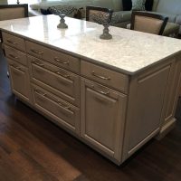 The Cambria Montgomery quartz countertops offers subtle whispers of soft blues and grays in a white background, atop a gray stained island. A double trash / recycle cabinet is integrated into abundant drawer storage space and island seating.