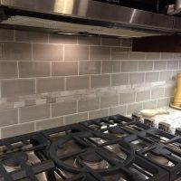 The gray subway tile is accented with a stone inlay, all uninterrupted by any electrical outlets (custom angled power strips provide ample outlets below the upper cabinets).