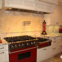 Bright red appliances add color and functionality to this chef's kitchen. Massive custom commercial style hood adorned with heavy carved wood accents. Storage of these frameless cabinets is maximized with lots of drawers and upper cabinet storage.