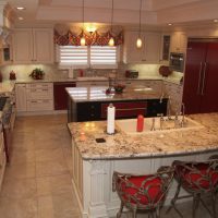 Traditional white kitchen with bright red appliances & accents & carved accents. Two islands and a double tray ceiling anchor the center of this chef's kitchen. Storage of these frameless cabinets is maximized with lots of drawers and upper cabinet storage.