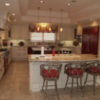 Traditional white kitchen with bright red appliances & accents & carved accents. Two islands and a double tray ceiling anchor the center of this chef's kitchen. Storage of these frameless cabinets is maximized with lots of drawers and upper cabinet storage.