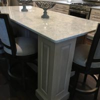 The Cambria Montgomery quartz countertops offers subtle whispers of soft blues and grays in a white background, atop white cabinets and a gray island.