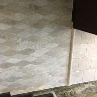 The backsplash consists of travertine tiles in a combination of wave and 4x4 staggered pattern. Also note the close-up of the quartzite countertop material.