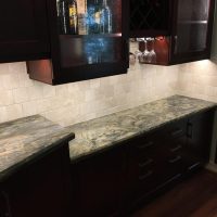 LED light strips provide continuous lighting below the upper cabinets and inside the glass-door cabinets. Note that there are no unsightly outlets or switches in these beautiful backsplashes; all the outlets are cleverly concealed below the upper cabinets. Gorgeous Fusion quartzite countertops add excitement to the dramatic dark cherry cabinets.