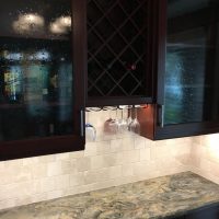 LED light strips provide continuous lighting below the upper cabinets. Note that there are no unsightly outlets or switches in these beautiful backsplashes; all the outlets are cleverly concealed below the upper cabinets. Gorgeous Fusion quartzite countertops add excitement to the dramatic dark cherry cabinets