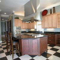 This transitional kitchen blends old with new and light with dark wood finishes, and features high-end Wood-Mode custom cabinetry with furniture detailing, black & white checkerboard floor, and high-end stainless steel appliances.