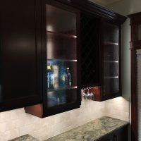 LED light strips provide continuous lighting below the upper cabinets and inside the glass-door cabinets. Note that there are no unsightly outlets or switches in these beautiful backsplashes; all the outlets are cleverly concealed below the upper cabinets. Gorgeous Fusion quartzite countertops add excitement to the dramatic dark cherry cabinets.